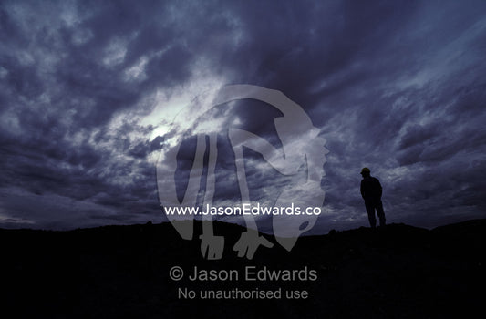 Silhouette of opal miner standing on slurry heap with storm clouds. Coober Peedy, South Australia.