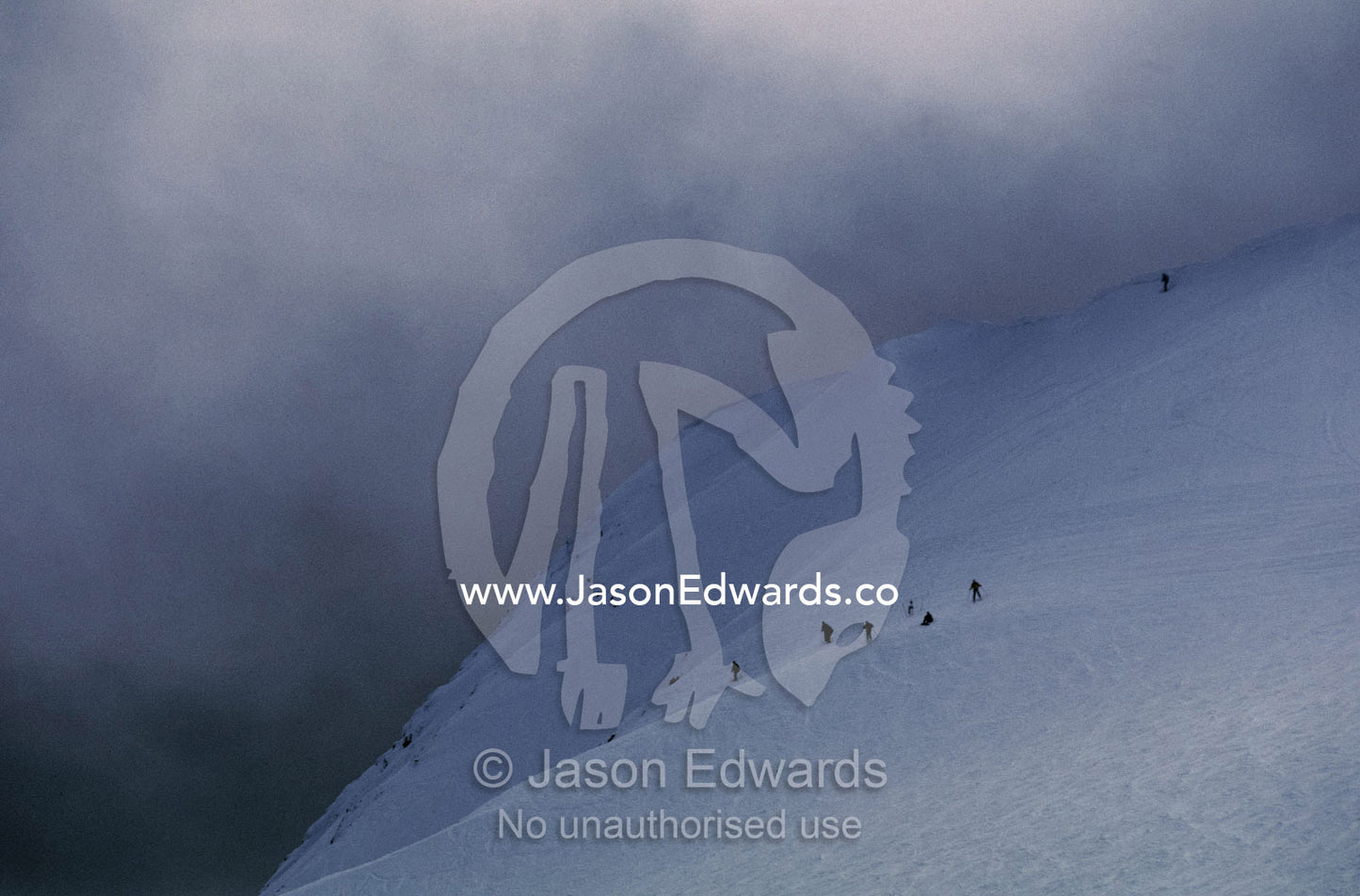 Menacing storm clouds loom over downhill snow skiers on a mountainside Mount Buller, Victoria, Australia.