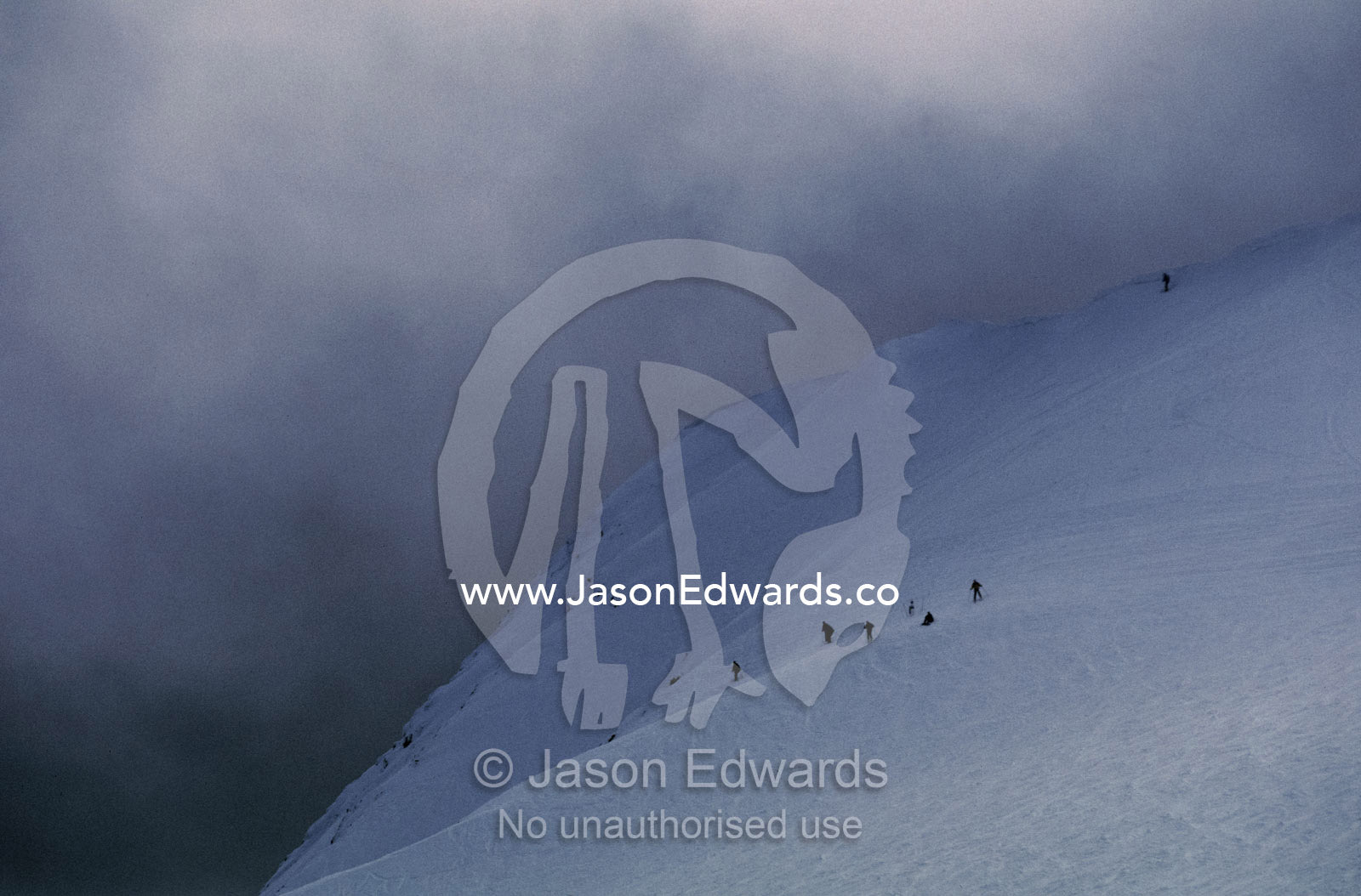 Menacing storm clouds loom over downhill snow skiers on a mountainside Mount Buller, Victoria, Australia.