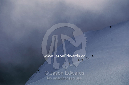 Menacing storm clouds loom over downhill snow skiers on a mountainside Mount Buller, Victoria, Australia.