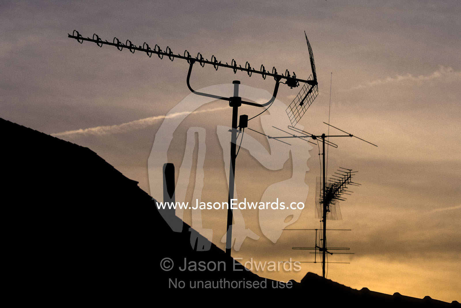 Silhouetted television antennas reach into the suburban sky at sunset. Tubingen, Baden-Wurttenberg, Germany.