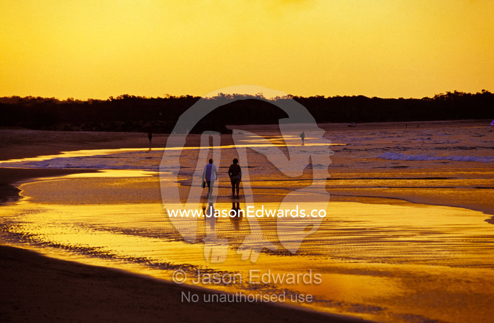 A couple going for a romantic walk on the beach at sunset. Noosa, Queensland, Australia.
