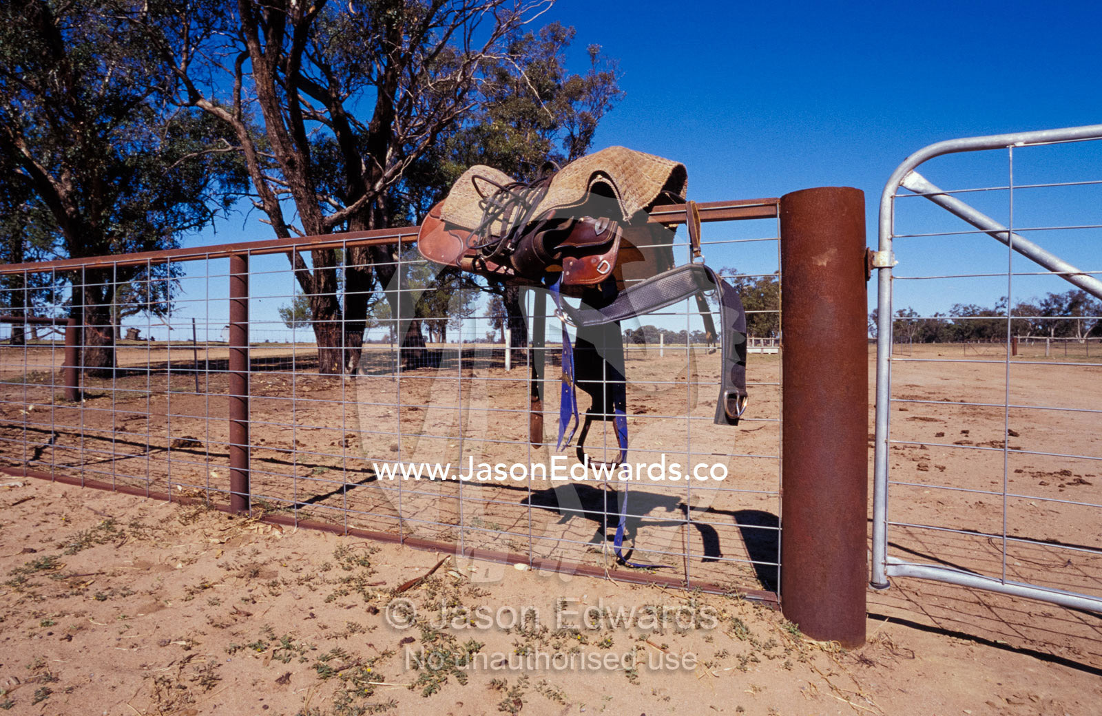 A horse saddle, stirrup and blanket looped over a cattle yard fence. Mundiwa Station Dennilquin, New South Wales, Australia.