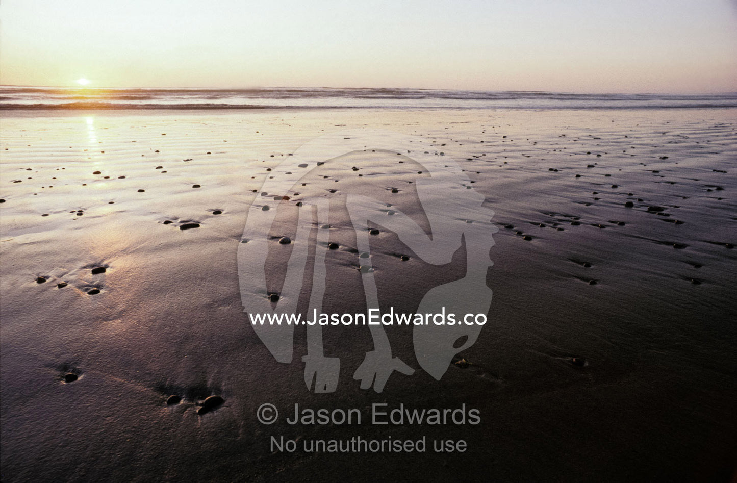 Pebbles form patterns on a sandy ocean tidal flat at sunset. Ocean Beach, Strahan, Tasmania, Australia.