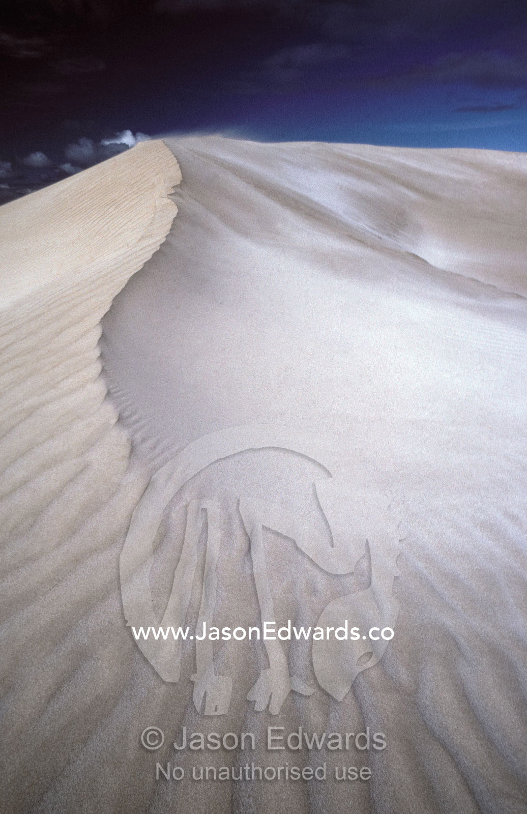 A vast coastal, white gleaming sand dune against a hazy blue sky. Fowlers Bay, South Australia.