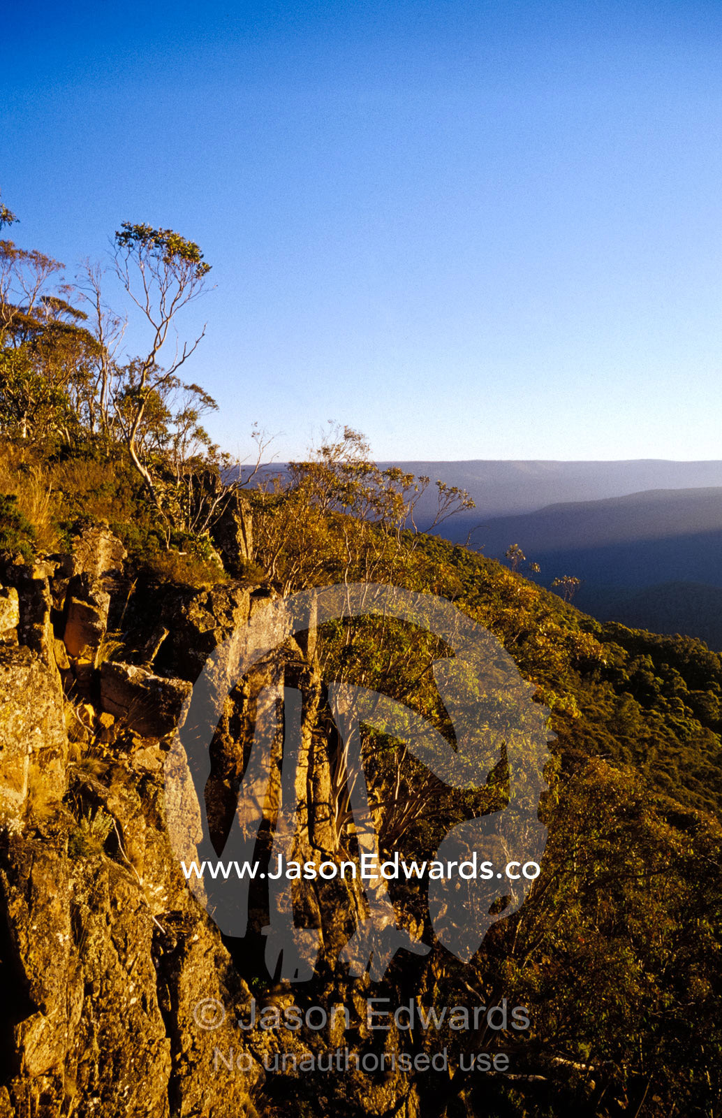 A rocky cliff face overlooking Alpine mountain ranges at sunset. Precipice Point Alpine National Park, Victoria, Australia.