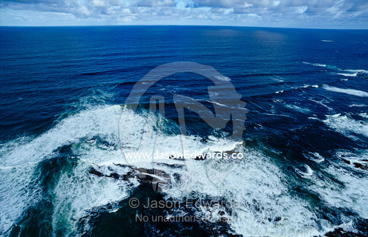 Waves smashing onto a rugged remote coastline beneath storm clouds. South West Conservation Area, Tasmania, Australia.