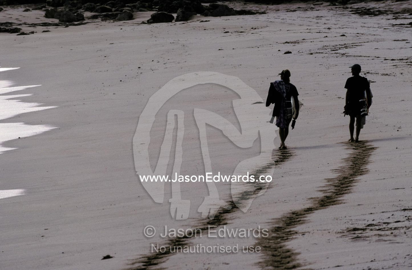 The silhouette of two surfers and their foot prints on a sandy beach. Cactus Beach, South Australia.