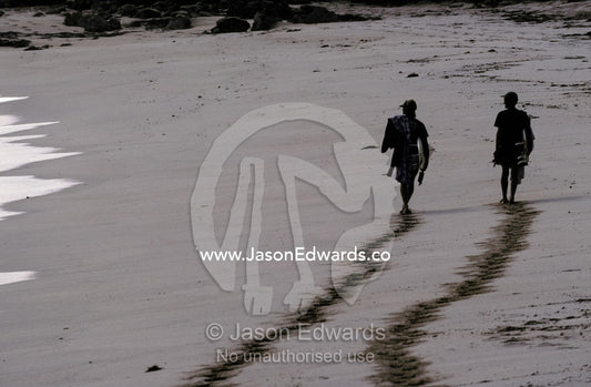 The silhouette of two surfers and their foot prints on a sandy beach. Cactus Beach, South Australia.