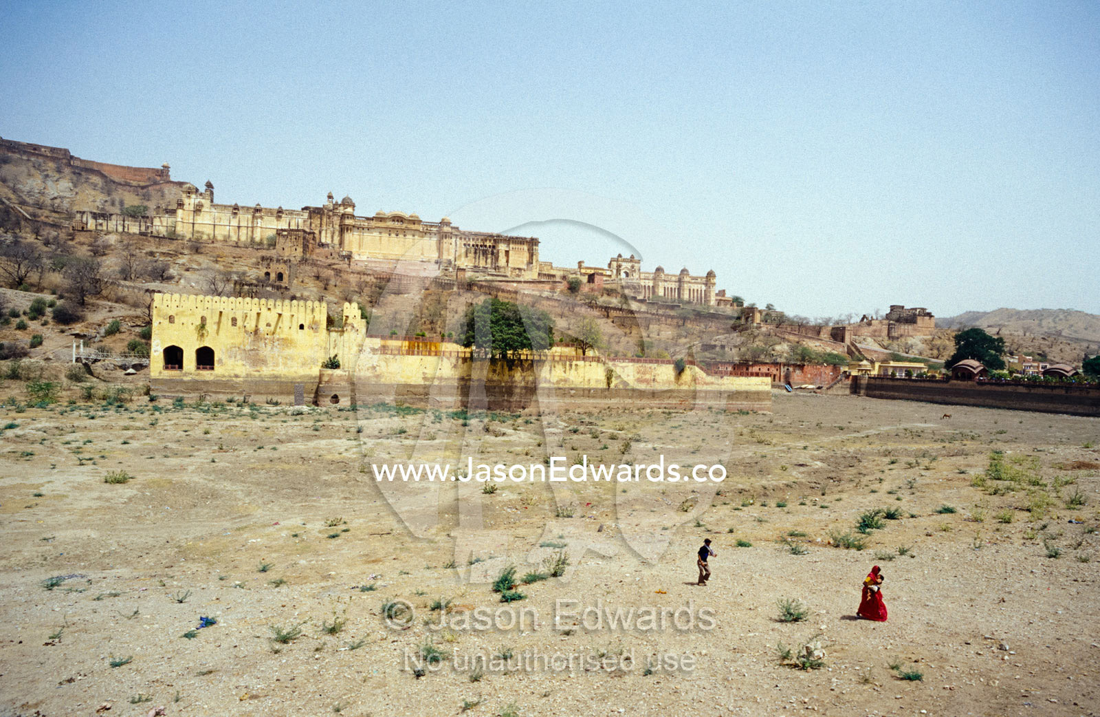 A woman with a baby and child crosses a dry lake bed in drought. Amber Fort Jaipur, India