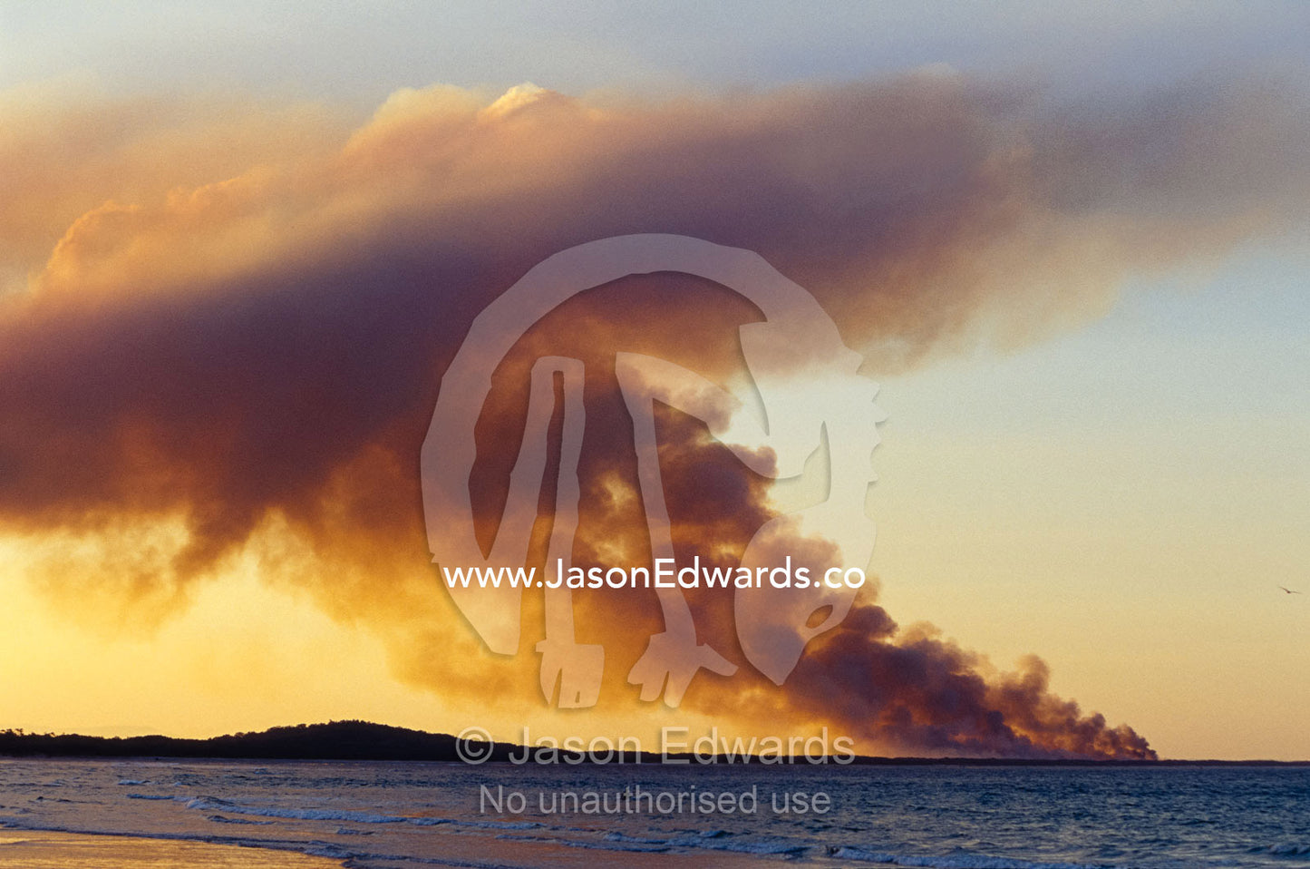 Smoke from a wildfire billows across a calm Bay at sunset. Noosa, Queensland, Australia.