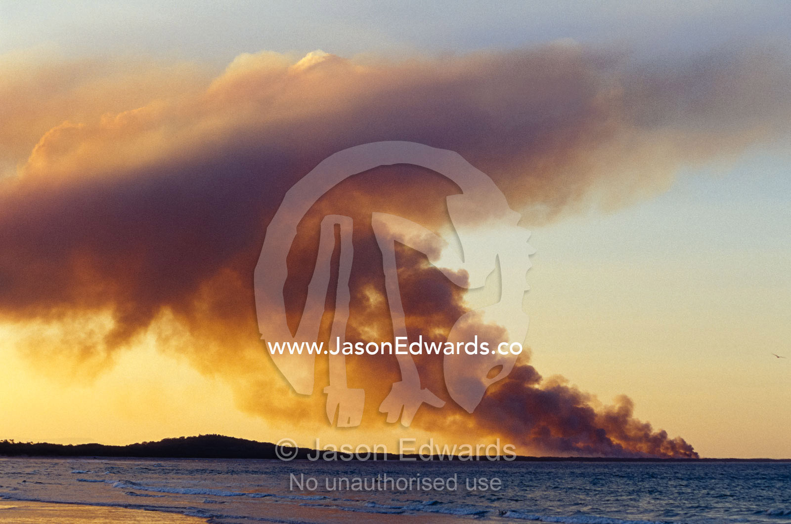 Smoke from a wildfire billows across a calm Bay at sunset. Noosa, Queensland, Australia.