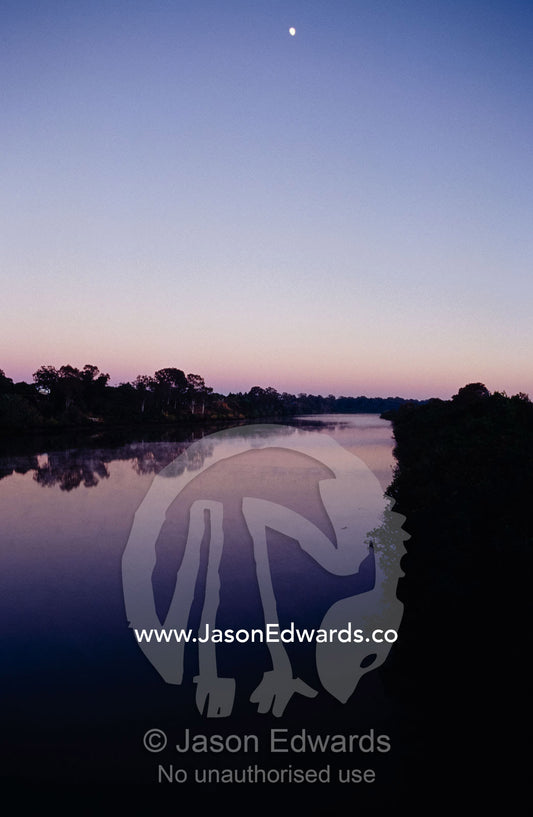 The moon high in a vast empty night sky pre-dawn over a calm river. Maryborough, Queensland, Australia.
