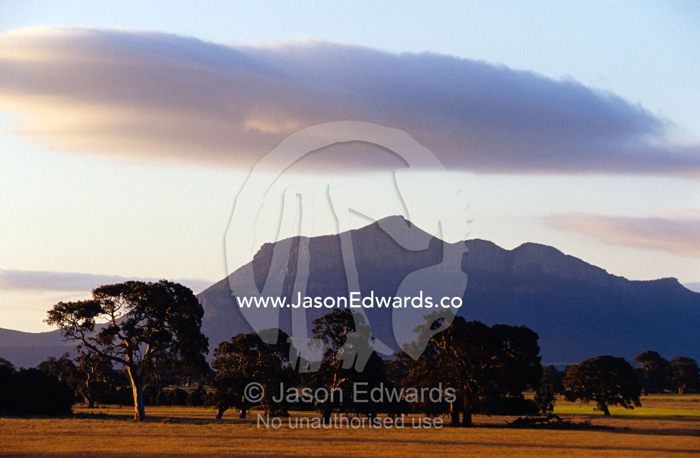 Picturesque mountain ranges loom over farmland plains at sunset. Grampians National Park, Victoria, Australia.