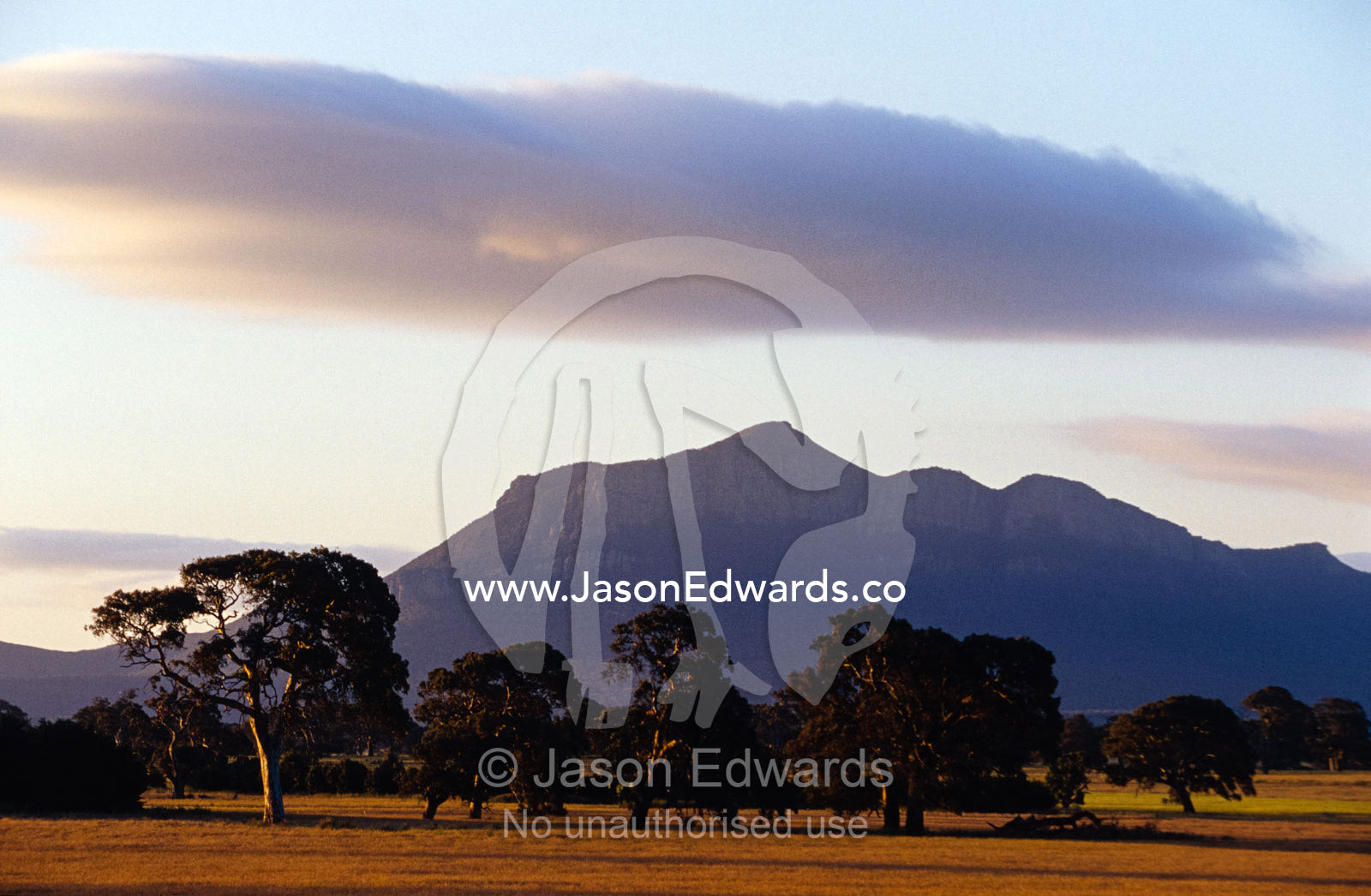 Picturesque mountain ranges loom over farmland plains at sunset. Grampians National Park, Victoria, Australia.