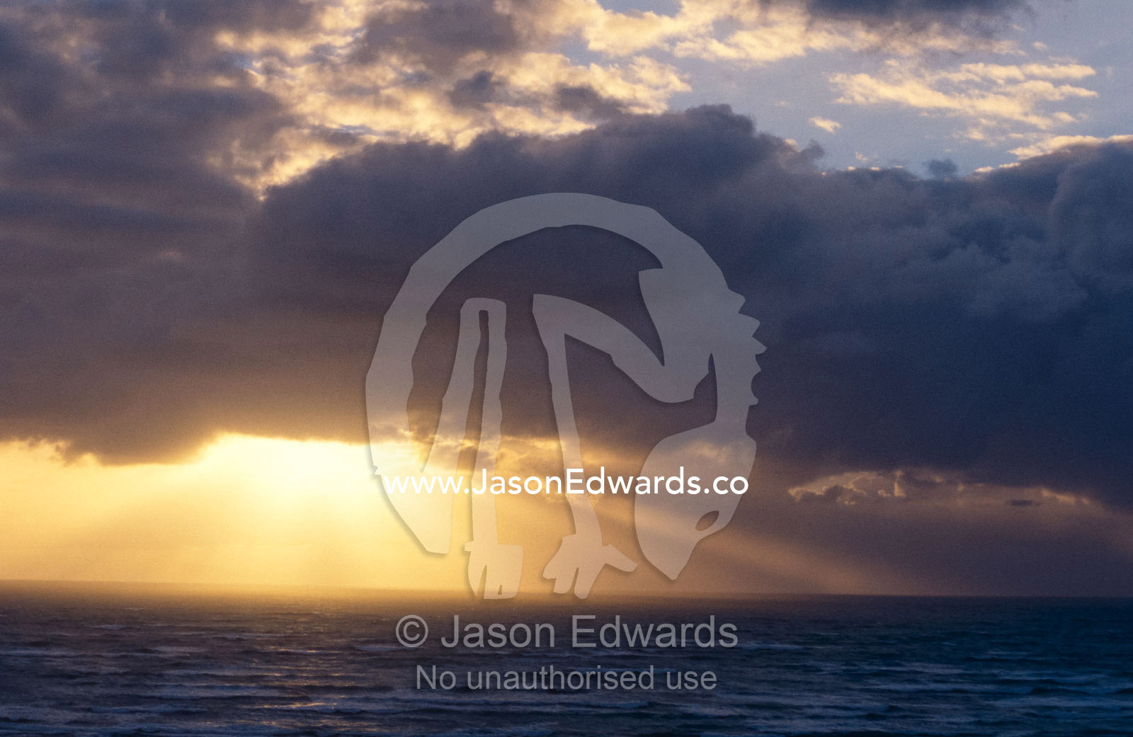 Sun rays pierce storm clouds over a vast southern ocean at sunset. Coorong National Park, Younghusband Penninsula, South Australia.
