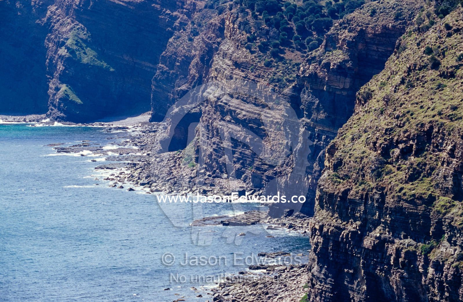 A rugged and eroded sheer cliff face towers over a calm ocean. Hummocky, Kangaroo Island, South Australia.