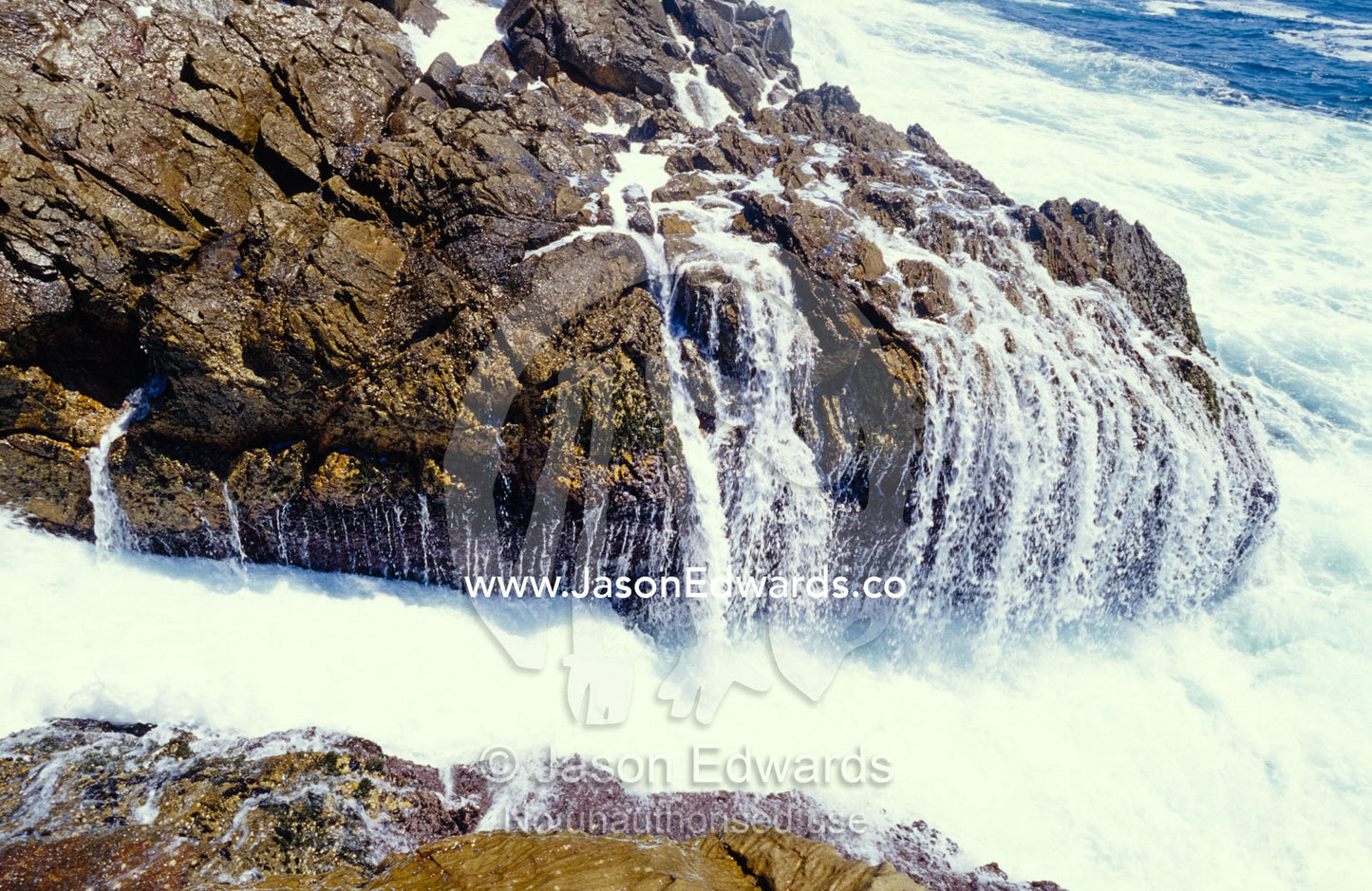 Ocean waves crashing onto rocks flow back into the sea. Tathra, New South Wales, Australia