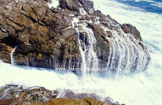 Ocean waves crashing onto rocks flow back into the sea. Tathra, New South Wales, Australia