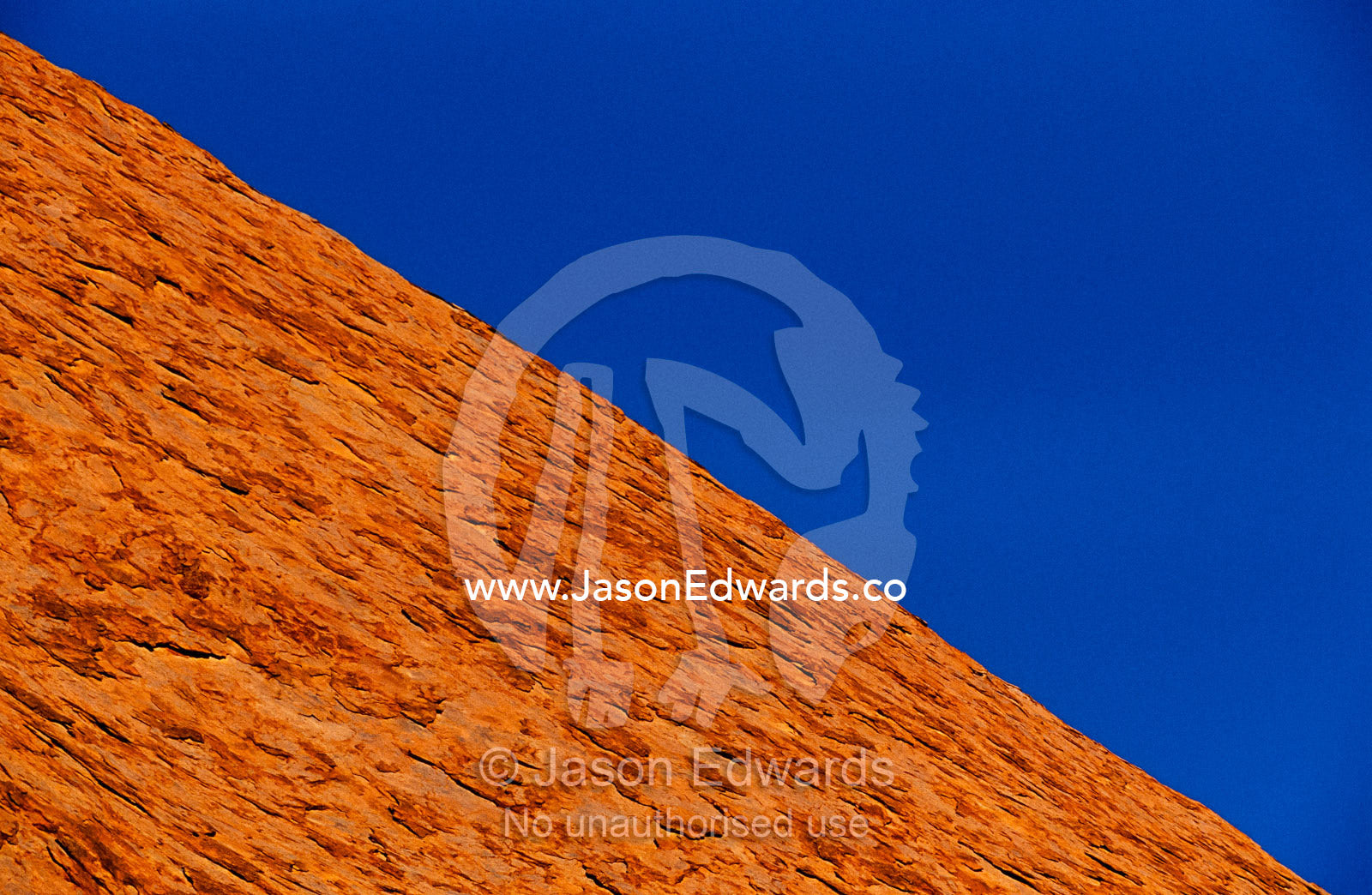 Uluru rock's oxidized rusty sandstone cliff and a blue sky. Uluru National Park, Northern Territory, Australia.