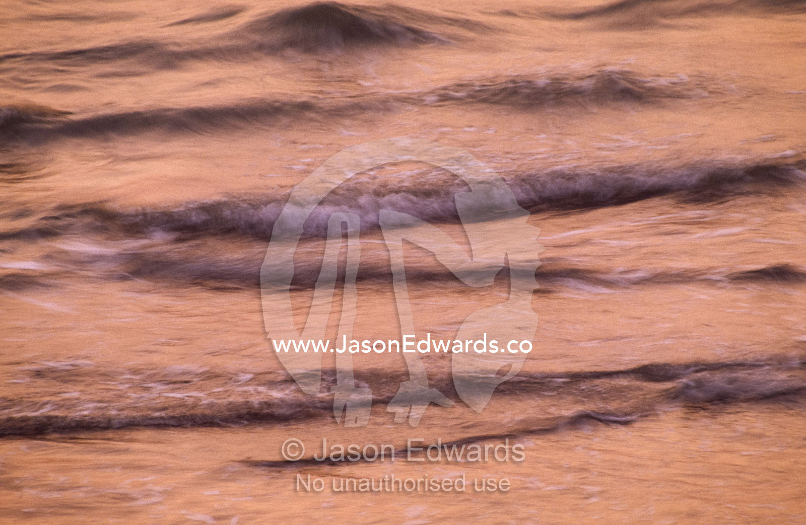 Lapping ocean waves bathed in the pink light of sunset afterglow. Darwin, Northern Territory, Australia.