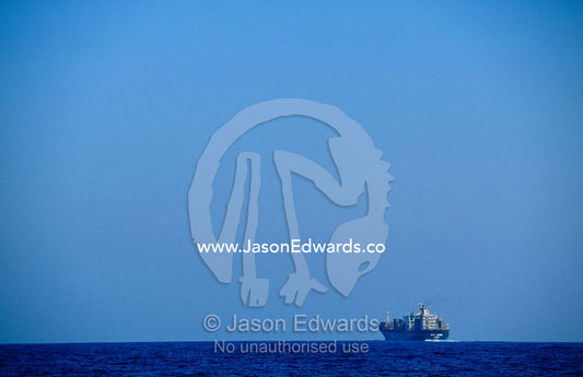 A cargo ship steaming across the calm ocean toward the horizon. Continental Shelf off Eden, New South Wales, Australia.