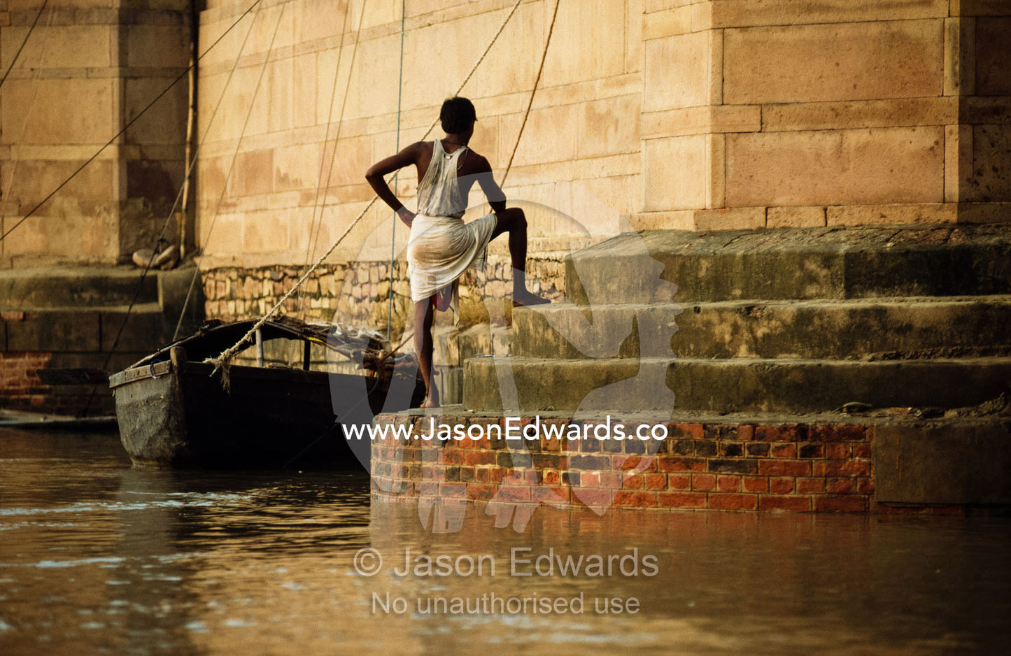 A pilgrim on the steps of a bathing ghat on the Ganges River at dawn. Varanasi, India.