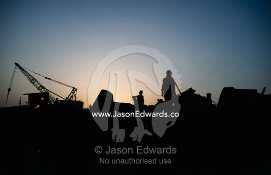 Silhouettes of laborers at a shipbreaking yard at sunset. Alang Ship Breaking Yards, Gujarat State, India.
