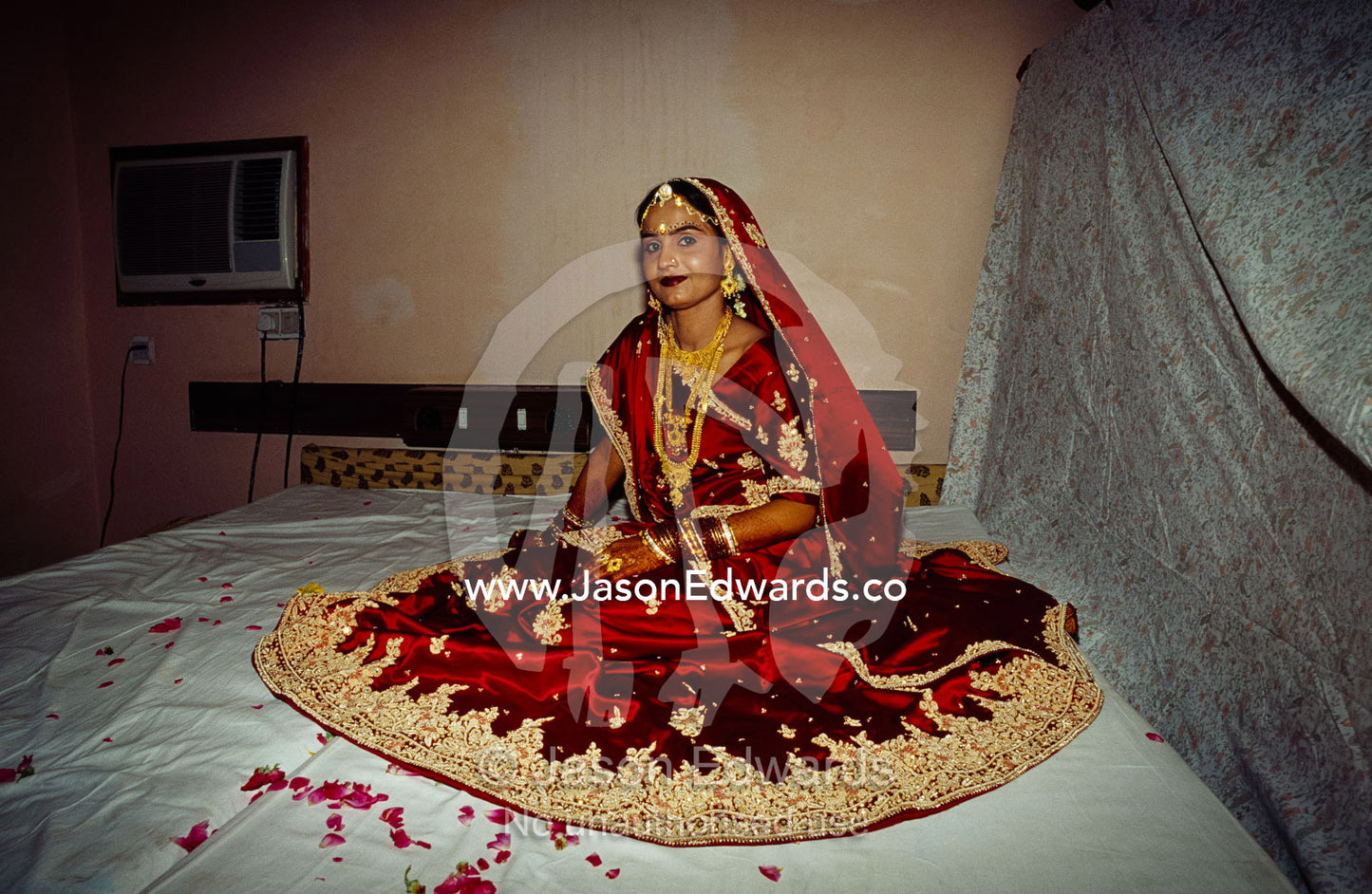 A bride in a red and gold silk sari awaits her wedding ceremony. Sawai Madhopur, Rajasthan State, India.