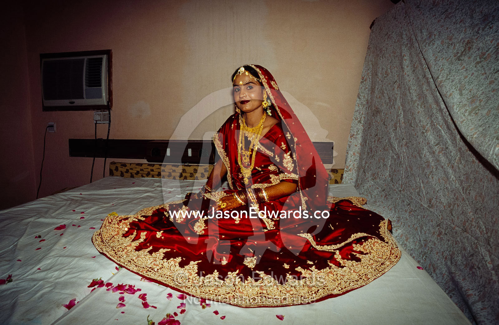 A bride in a red and gold silk sari awaits her wedding ceremony. Sawai Madhopur, Rajasthan State, India.