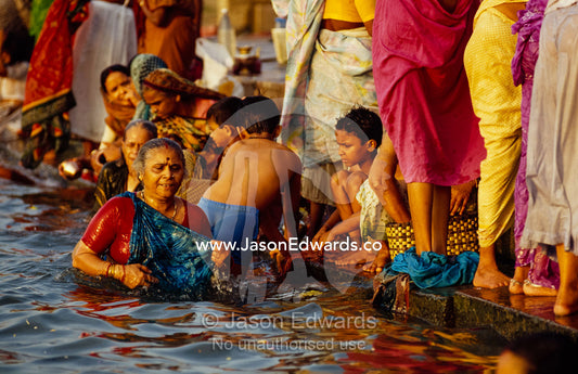Women and their sons bathe in the Ganges River to remove sins. Varanasi (Benares), India.