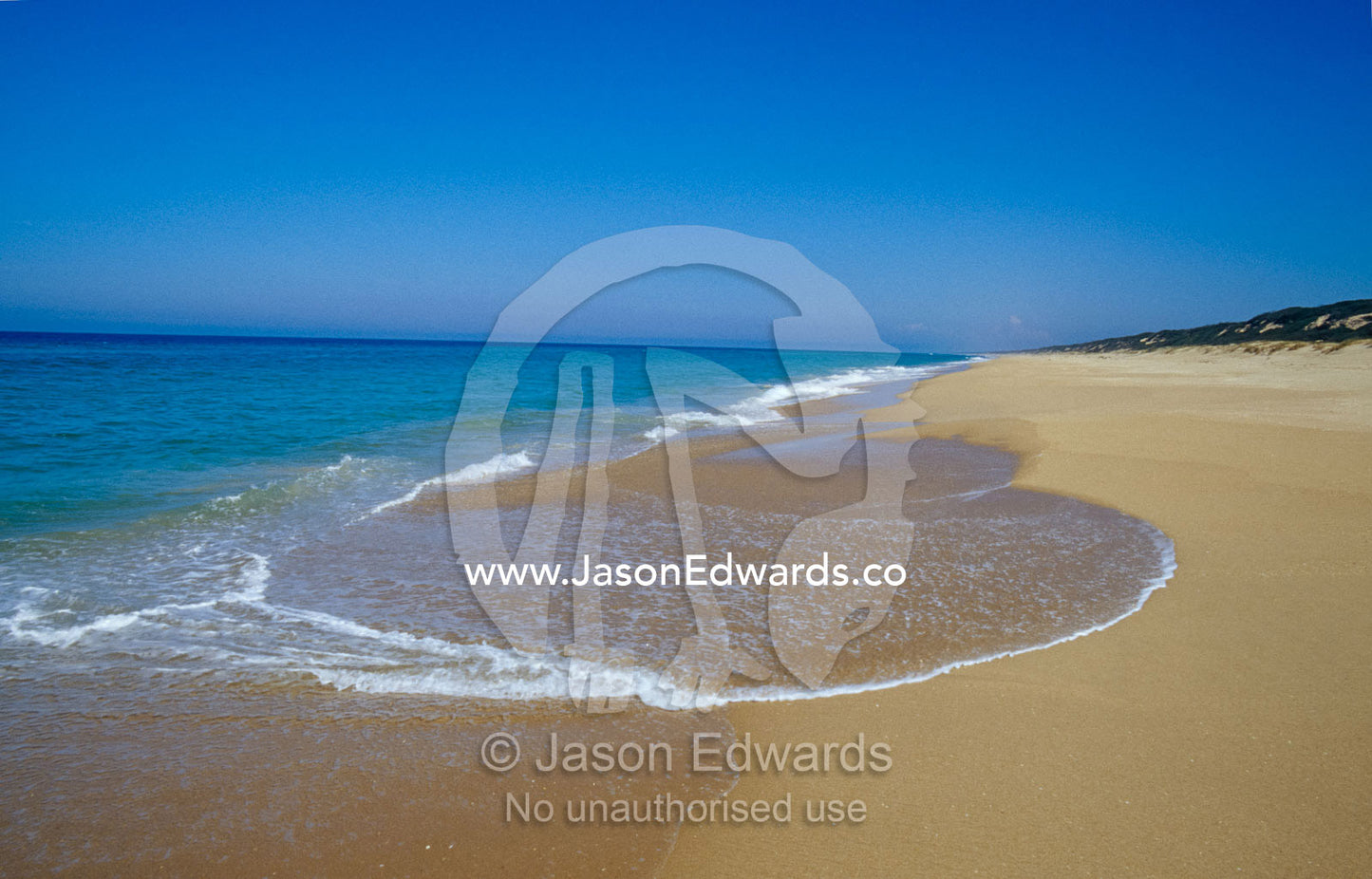 A deep blue sea and crisp waves lap the shoreline of the 90 Mile Beach The Lakes National Park, Victoria, Australia.