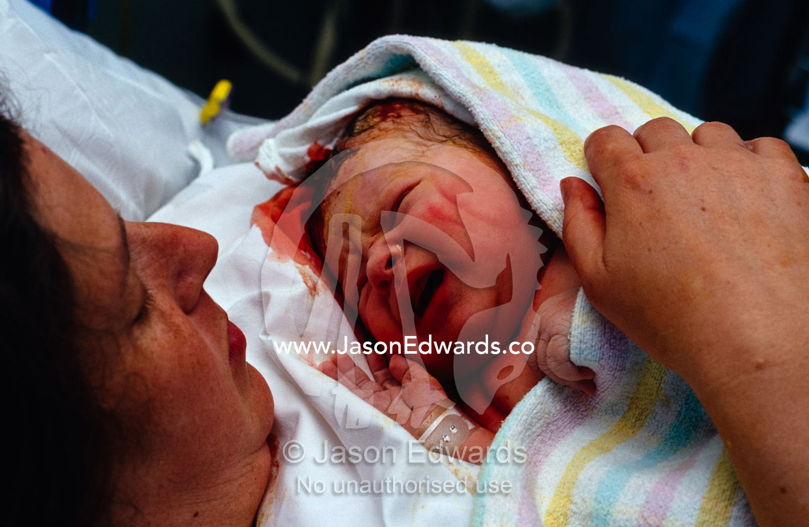 A mother nestles her newborn baby boy in a blanket against her chest. Carlton, Victoria, Australia.