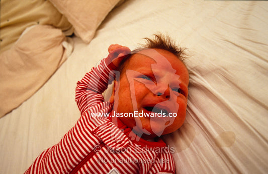 A one month old baby hungry and a little frustrated lying on a bed. North Carlton, Victoria, Australia.