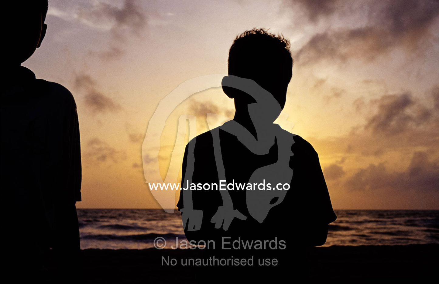 Two young boys watch the sunset on a tropical island beach. Negombo Beach, Sri Lanka.