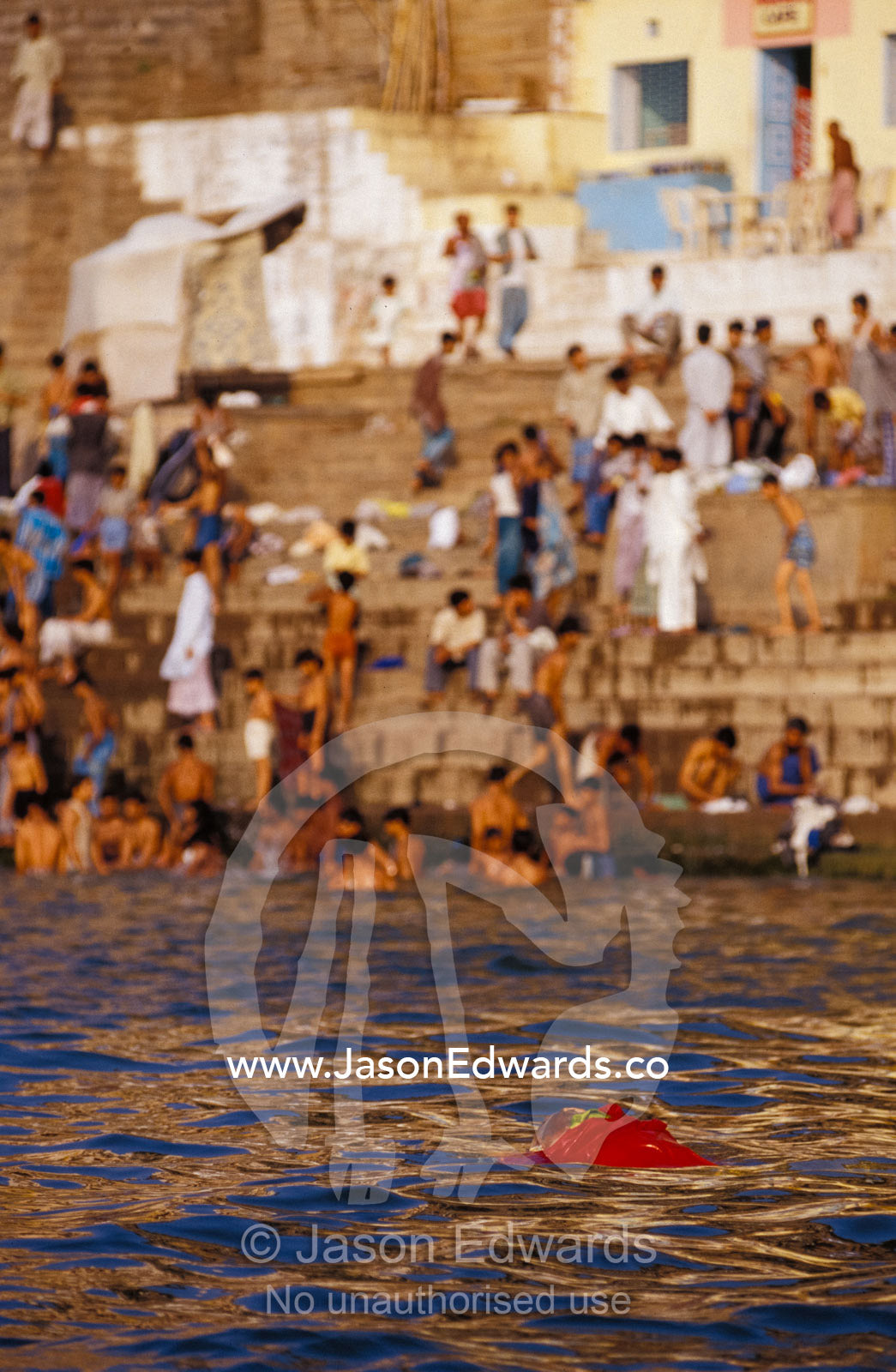 A dead holy man floats past pilgrims bathing in the Ganges River. Varanasi, Uttar Pradesh, India.