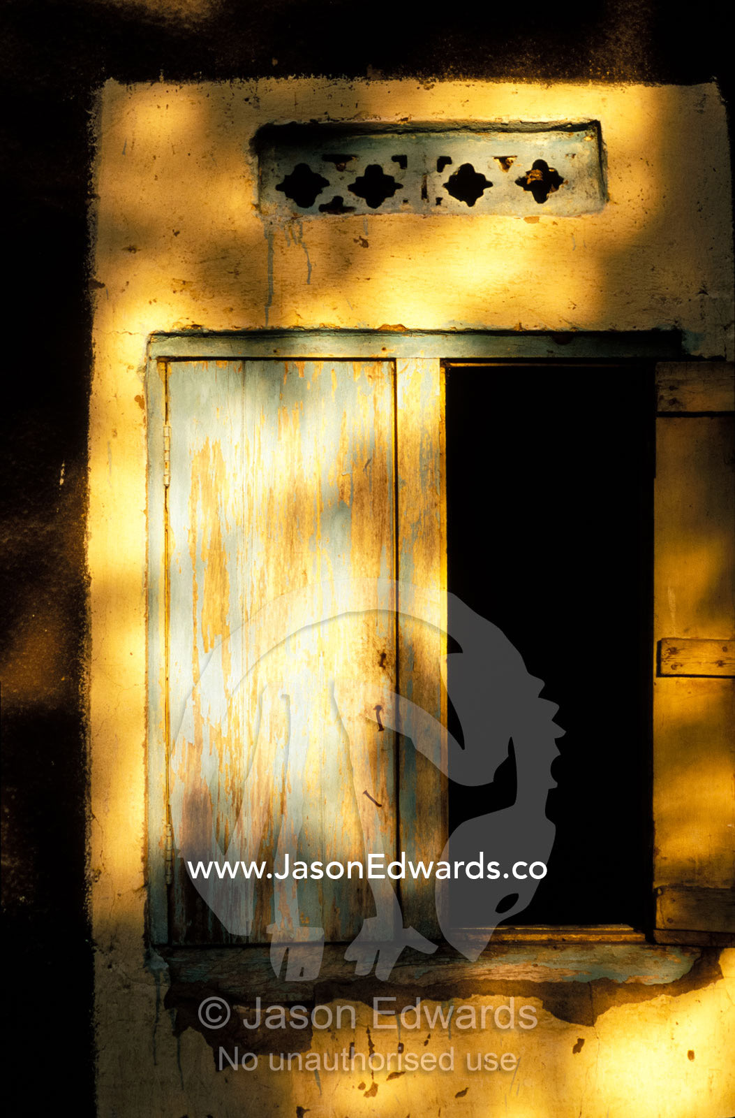 Sunset shadows fall on the painted shutters of a village hut window. Tororo District, Uganda.