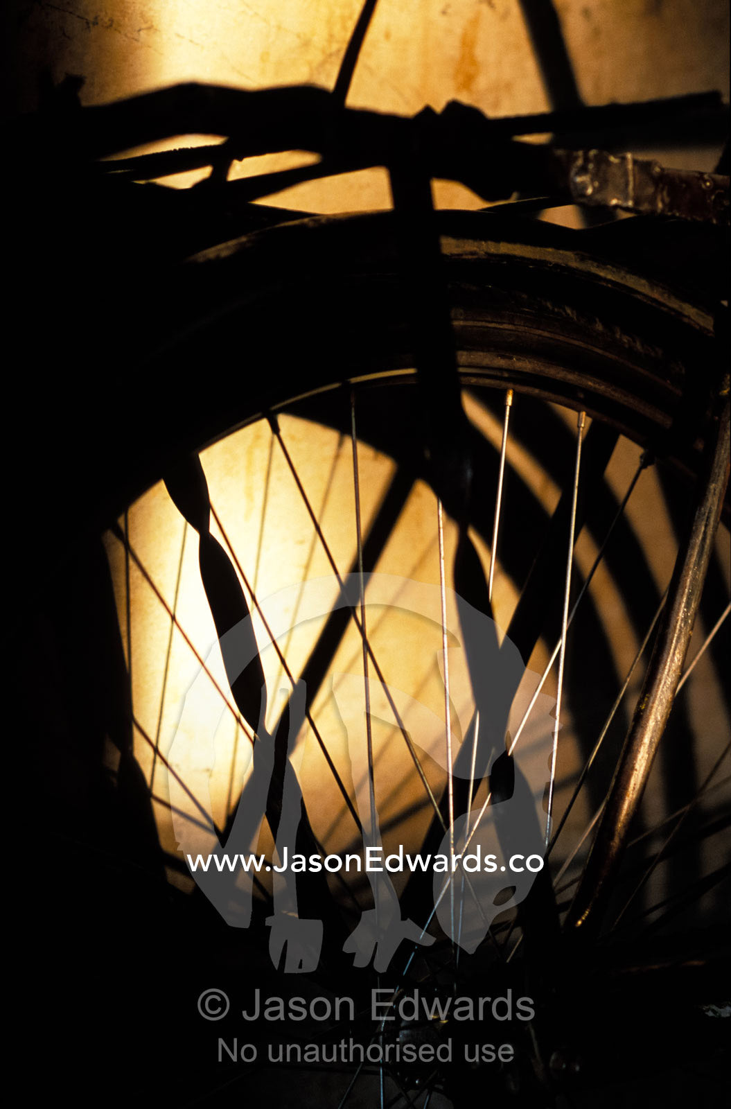 Sunset falls over the wheel of a bike casting shadows on a hut. Tororo District, Uganda.