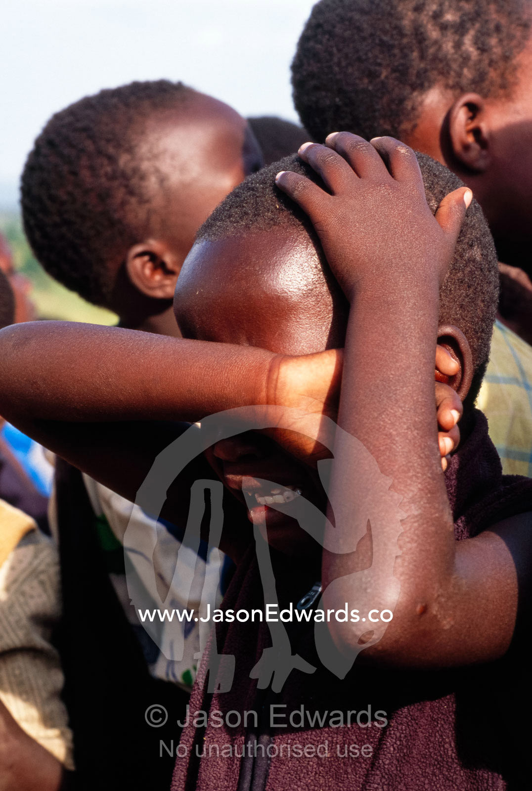 An African school child shielding his eyes whilst crying during class. Tororo Prison School, Tororo District, Uganda.