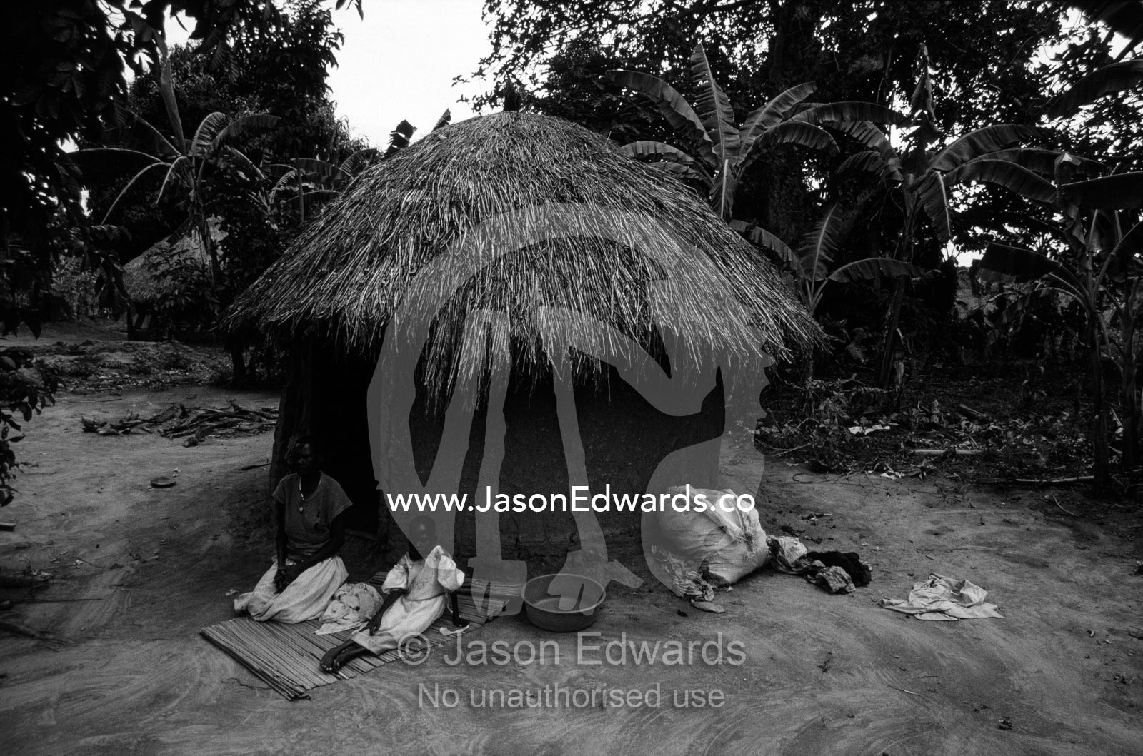 An orphaned African girl with her grandmother and their thatched hut. Tororo District, Uganda.