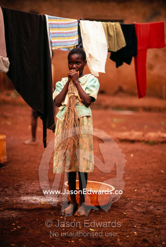 A young girl pauses between cleaning duties in an African village. Tororo District, Uganda.