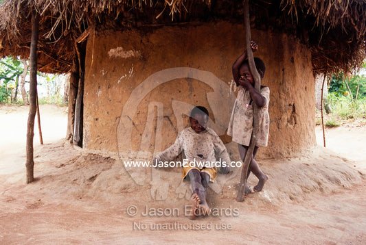 Village children rest in the shade of a hut from the afternoon heat. Tororo District, Uganda.