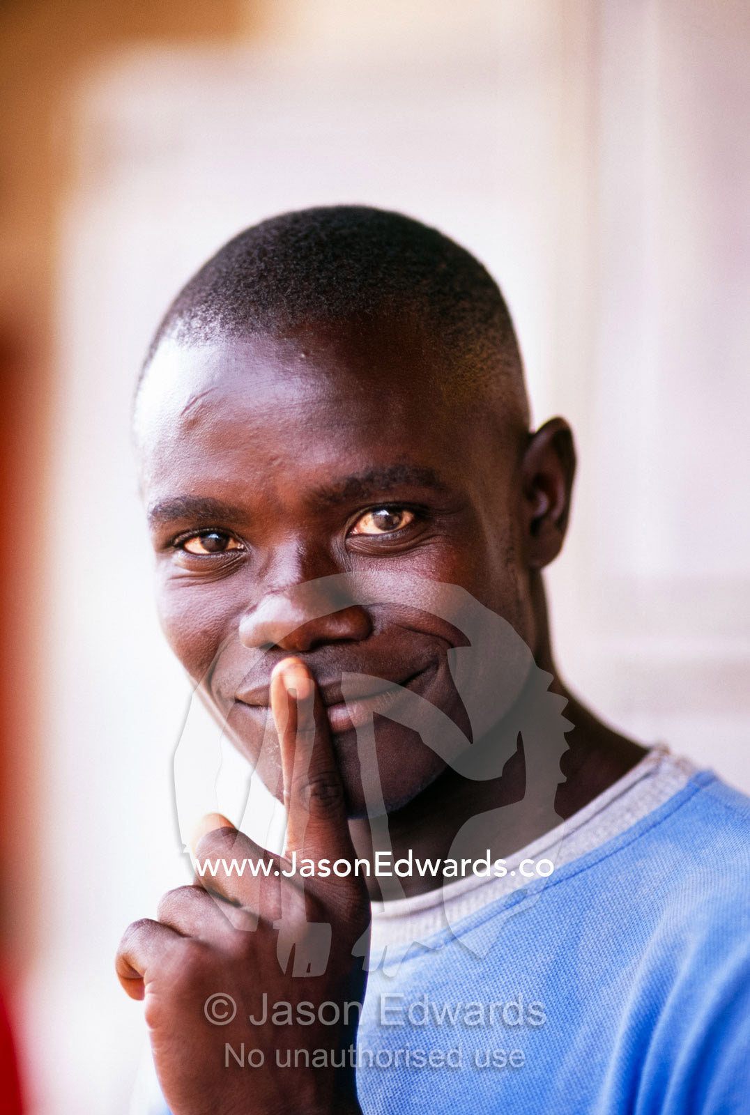 A young Ugandan man signals silence with his finger on his lips. Tororo District, Uganda.
