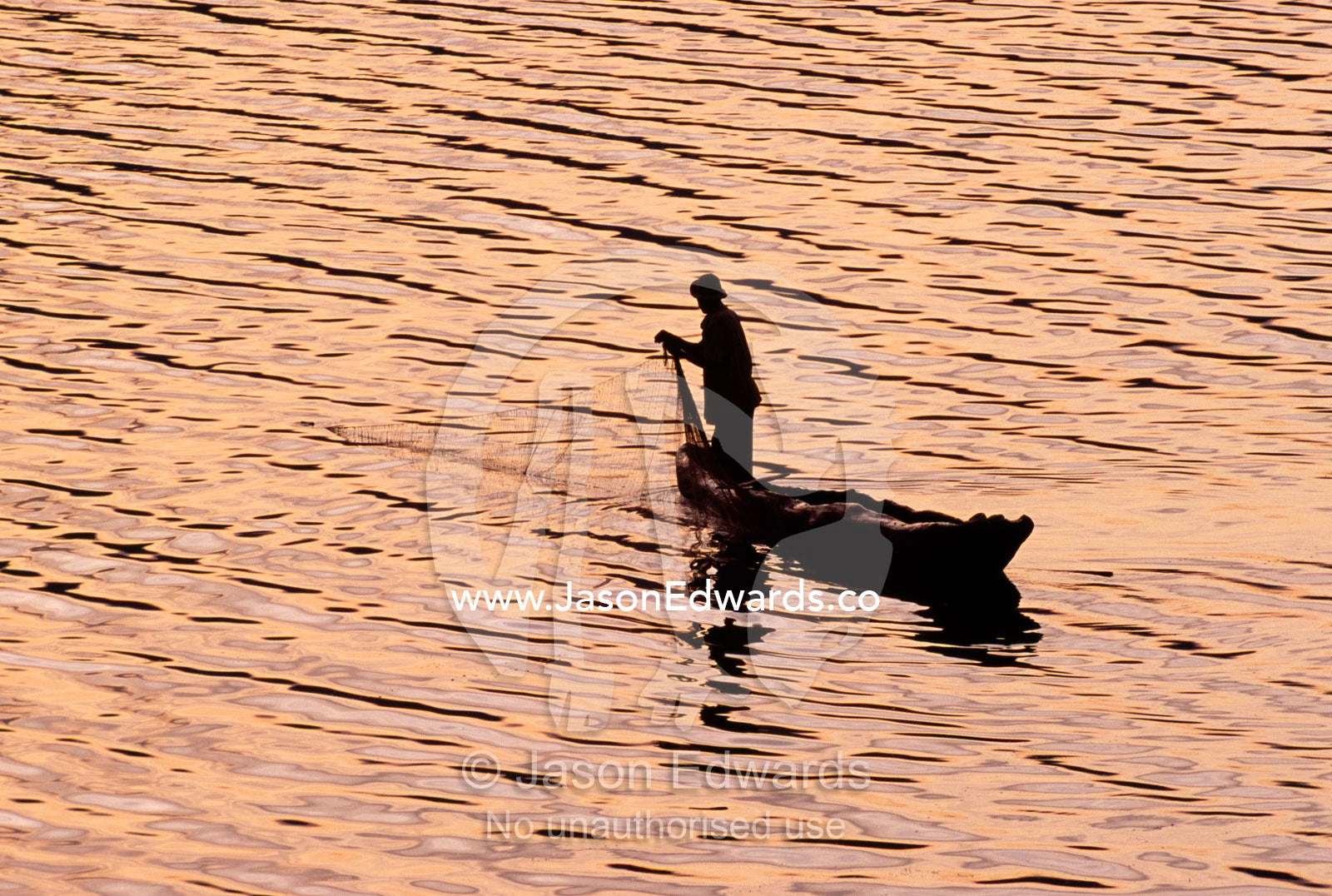 A lone fisherman casts his nets into a still volcanic lake at dawn. Lake Mutanda, Kisoro District, Western Uganda.