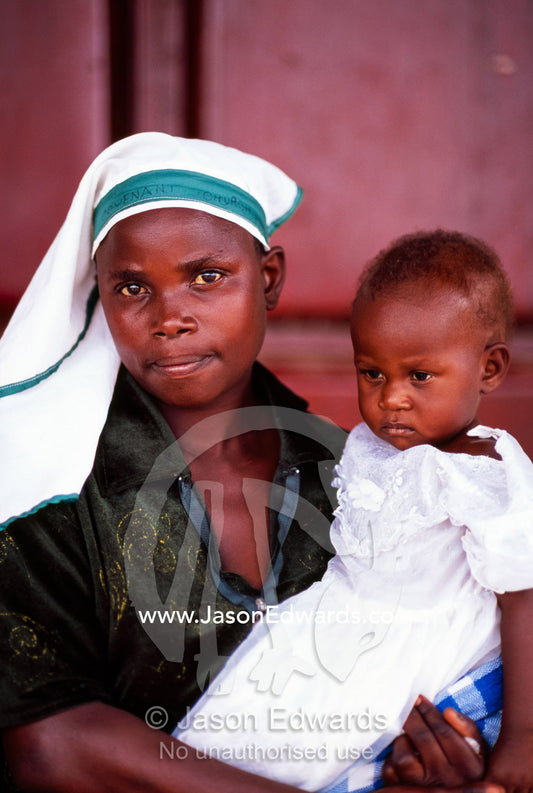 A mother and daughter rest from the heat in the shade of a shop. Tororo District, Uganda.