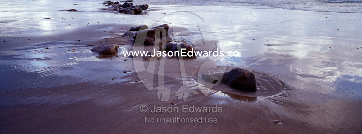 Storm clouds reflected in wet sand on a stony beach at low tide. Jan Juc, Victoria, Australia.