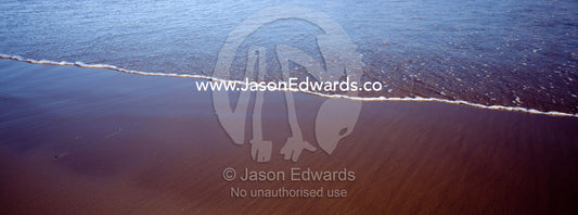 The leading edge of a wave creeps up onto the beach at low tide. Jan Juc, Victoria, Australia.