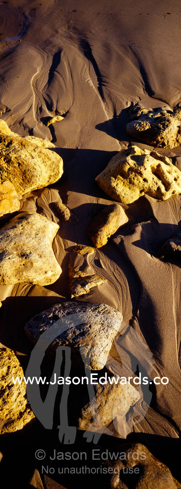 Waves leave beautiful patterns trailing behind boulders on a beach. Jan Juc, Victoria, Australia.