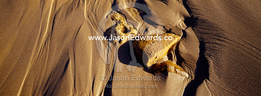 Waves leave beautiful patterns trailing behind boulders on a beach. Jan Juc, Victoria, Australia.