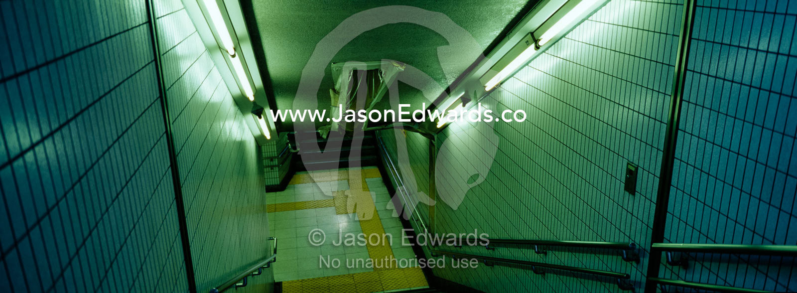 A stairwell illuminated by flourescent tubes descends to a subway. Ikebukuro Station, Tokyo, Japan.